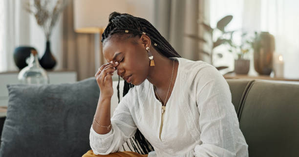 A woman sitting on a couch looking tired and stressed, holding her forehead